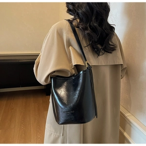 Close-up of a black leather bucket bag worn with a stylish beige trench coat in a cozy room