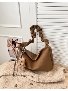 Detail of dark brown tote bag with ruffled strap and plush bear charm on soft rug