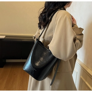 Detail of high-quality black glossy leather bucket bag with embossed logo and adjustable strap