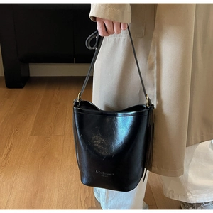 Detail showing the glossy black bucket bag with a stylish adjustable shoulder strap