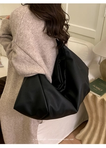 Detail shot of a large black leather tote bag with soft pleats on a model in a cozy room