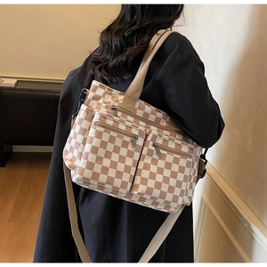 Detail of checkered tote bag showing zip pockets and adjustable shoulder strap worn by model