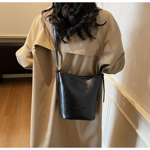 Detail view of a black leather bucket bag with fashion text and adjustable shoulder strap