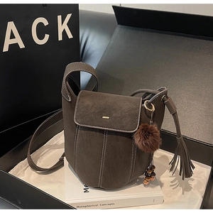 Dettaglio di una borsa a secchiello in pelle scamosciata marrone con cuciture e nappine