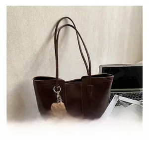 Detail of dark brown tote bag with vertical stripes and cute plush bear charm on a desk