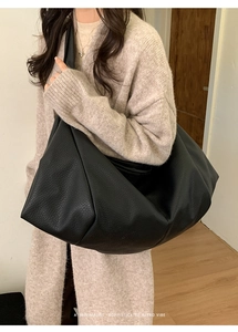 Chic black pleated hobo bag in grainy leather texture shown styled on a model's shoulder
