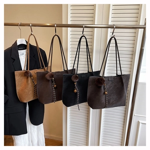 Detail view of large tote bags in four colors with plush ball charms on a metal rack