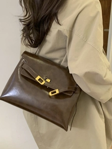 Minimalist deep brown leather tote bag with gold metal buckle shown on a trench coat