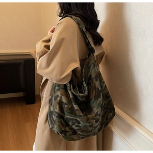 Detail shot of the large camouflage canvas tote bag worn by a model in a trench coat