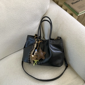 Détail d'un sac seau en cuir noir avec des breloques décoratives sur un canapé blanc