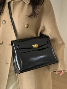 Minimalist black glossy leather tote bag with gold metal buckle shown on a model