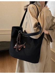 Grand sac cabas noir avec breloque chien en cuir porté à l'épaule par un mannequin en trench