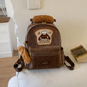 Detail of brown corduroy backpack featuring chef puppy embroidery and baguette charms
