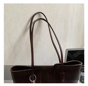 Detail of dark brown leather tote bag with fine stitching and sleek metal ring accent