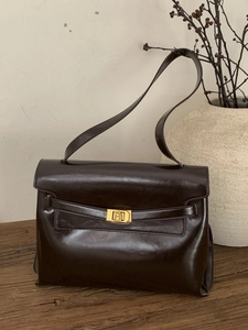Classic dark brown glossy leather tote bag with gold buckle on an elegant wooden stool
