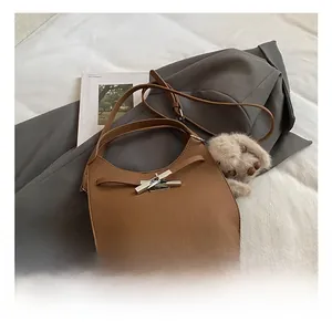 Detailed view of a brown leather hobo bag with a plush charm on a cozy neutral setting