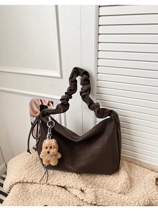 Detail of dark brown pleated tote bag with creative shoulder strap and plush dog charm