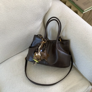 Vue détaillée du sac plissé marron avec charme d'ours sur un canapé blanc