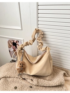 Close-up of beige pleated tote bag with a cute brown teddy bear plush charm on side