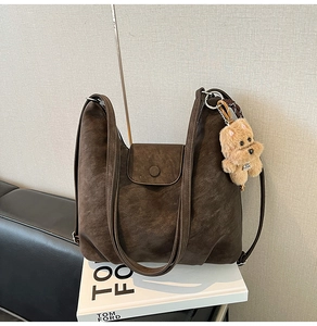 Detail view of brown vintage hobo bag with teddy bear pendant on white book base