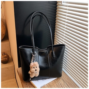 Close-up of black glossy leather tote bag featuring a teddy bear charm and sleek stitching
