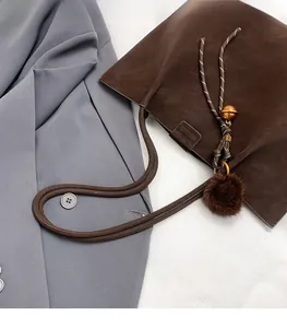 Detail of dark brown suede tote bag with decorative pompom and bell on grey blazer