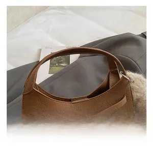 Detail of brown lychee grain leather bucket bag with silver metal buckle and plush pompom charm