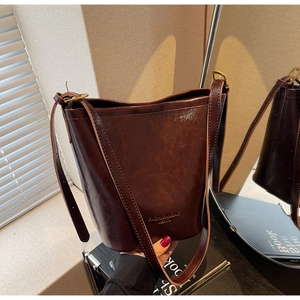 Detail of deep brown bucket bag in glossy oil-wax leather with adjustable gold strap buckle
