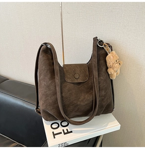 Close-up of a vintage dark brown tote bag with leather texture and a plush bear pendant