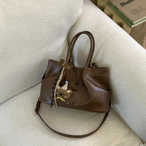 Détail du sac cabas en cuir marron foncé avec breloque ours et bandoulière sur un canapé