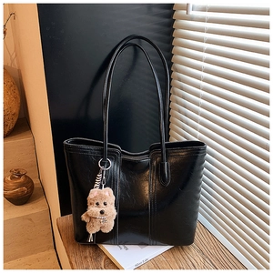 Detail of black faux leather tote bag with vertical stitching and brown bear charm