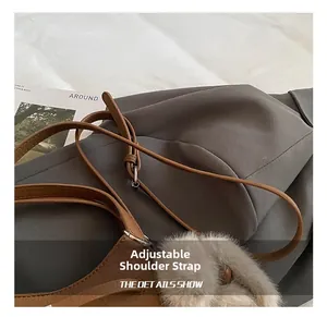 Detail view of brown leather handbag with adjustable strap and grey faux fur pompom charm