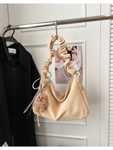 Detail of beige hobo bag featuring pleated shoulder strap and plush bear charm