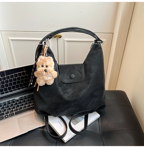 Detail of black faux leather tote bag with plush puppy charm on a city bench