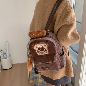 Close-up of brown corduroy backpack featuring a chef puppy patch and plush croissant charm