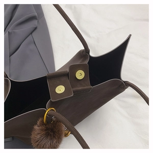 Detailed macro view of the magnetic buckle closure and plush charm on brown leather tote