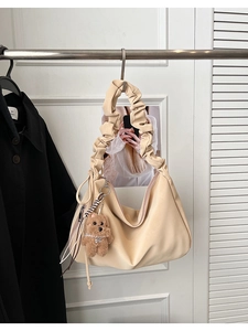 Close-up of cream tote bag featuring a pleated shoulder strap and plush bear charm