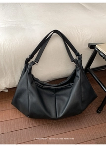 Close-up of black pleated leather tote bag with silver rings on dark wood floor