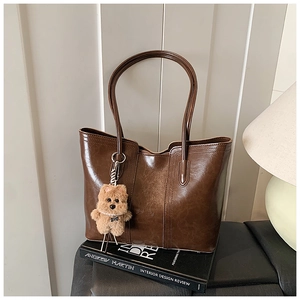 Detail of a brown tote bag with leather texture and a cute plush dog pendant