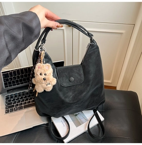 Close-up of a vintage black tote bag with leather texture and cute teddy bear charm