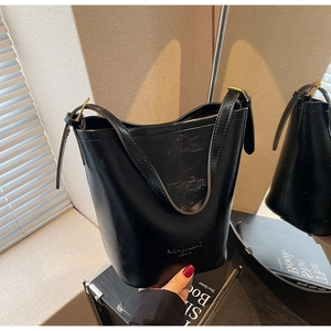 Detail of black bucket bag showing polished synthetic leather and gold hardware