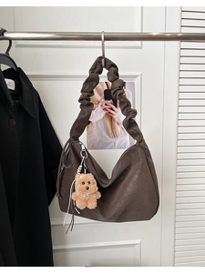 Detail of dark brown leather tote bag with ruched shoulder strap and cute teddy bear charm