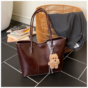 Detail of dark brown glossy leather tote bag featuring a cute plush puppy charm