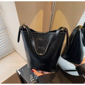 Detail of a black leather bucket bag with embossed text and gold metal hardware