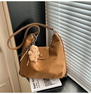 Detailed close-up of a brown faux leather shoulder bag with a cute plush bear charm accessory