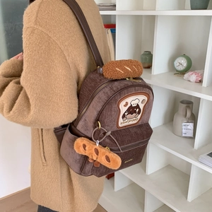 Close-up of brown corduroy chef puppy backpack with plush bread charms and leather straps