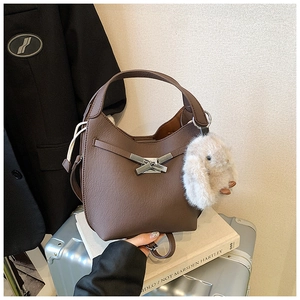 Detail view of brown bucket bag with lychee texture and cute rabbit charm on a suitcase