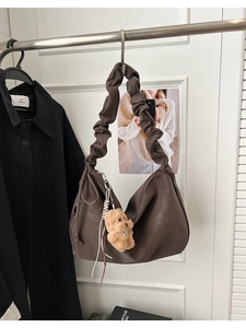 Detail of dark brown slouchy tote with ruched handle and plush bear pendant