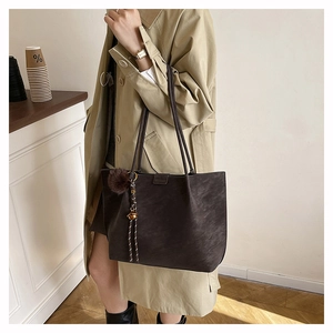 Detail of a large coffee brown tote bag in matte suede with tassel and pompom charm