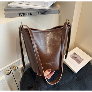 Detail of dark brown glossy leather bucket bag with gold hardware and logo embossing